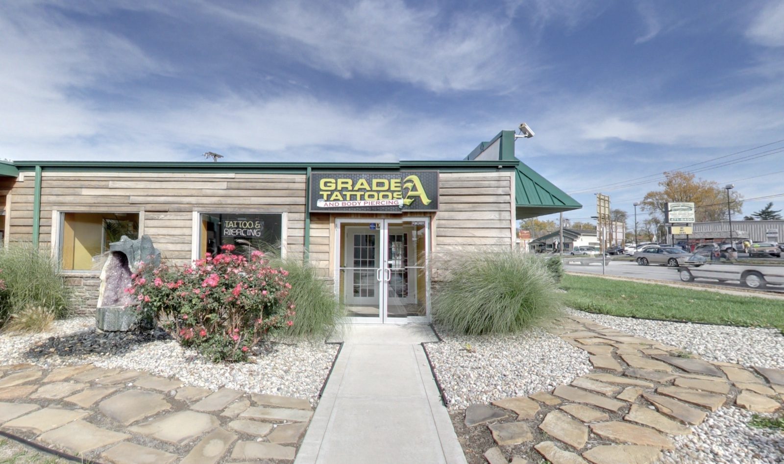 The Grade A Tattoos front entrance with a stone walkway, flowers, and landscaping